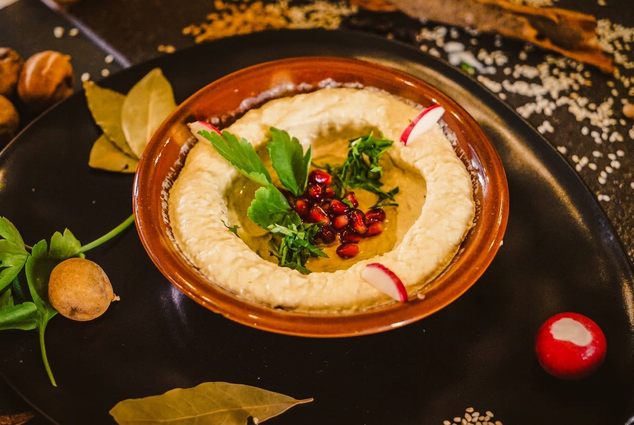 Hummus in einer Terrakotta-Schale mit Kräutern und Granatapfel